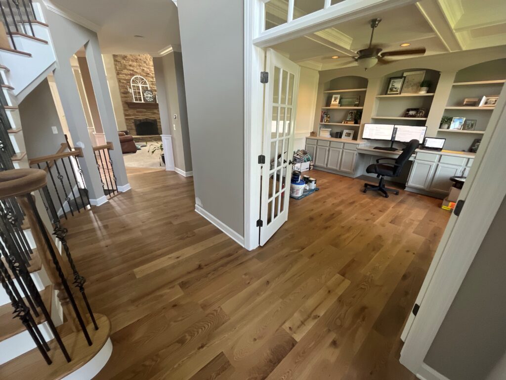 Home office with built-in wall bookshelves, hardwood floors, and neutral color palette