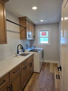 Modern laundry room with custom cabinetry, vinyl plank flooring, and matte black hardware accents