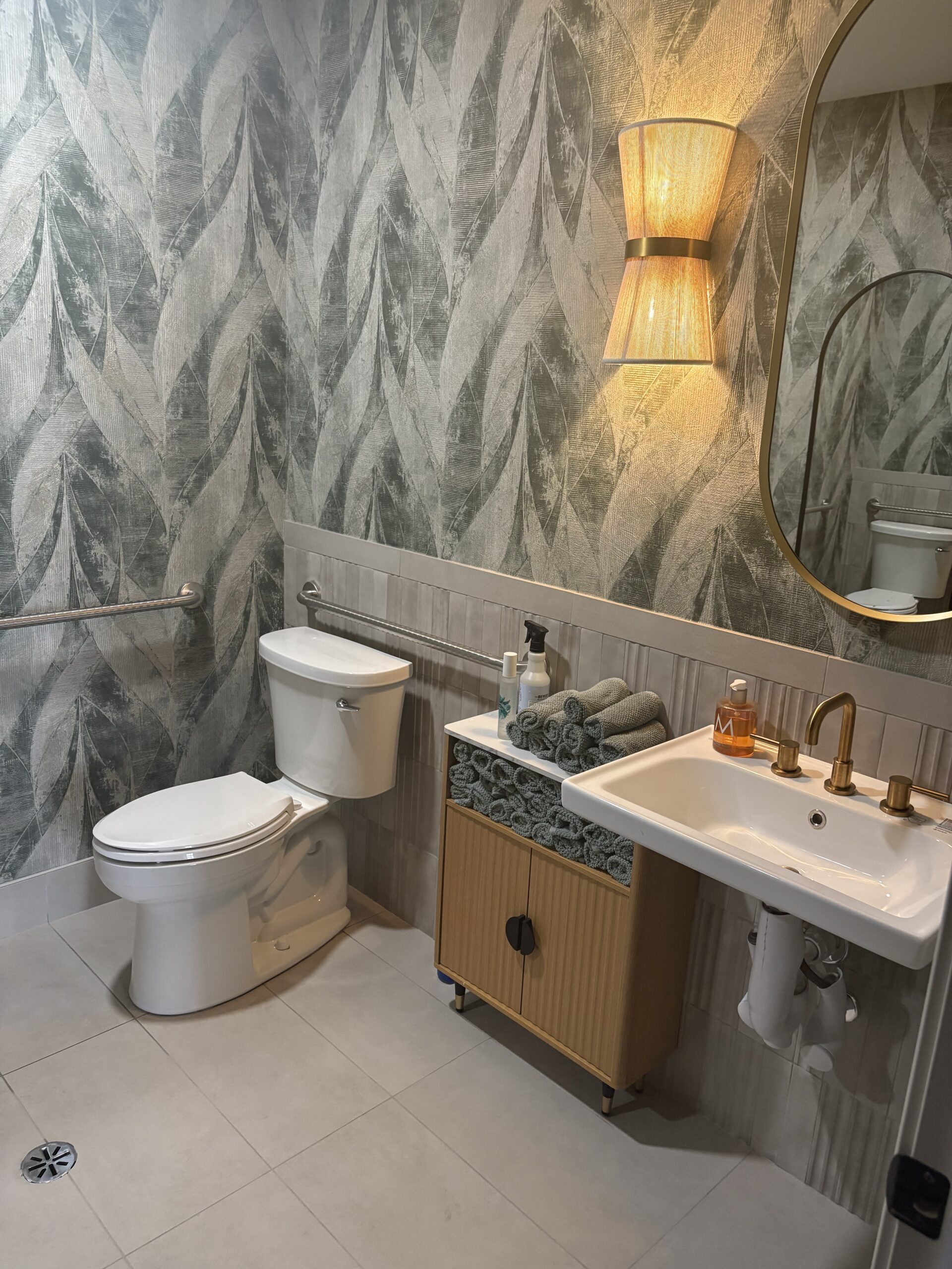 Stylish commercial restroom featuring decorative wallpaper, brass hardware, and elegant lighting