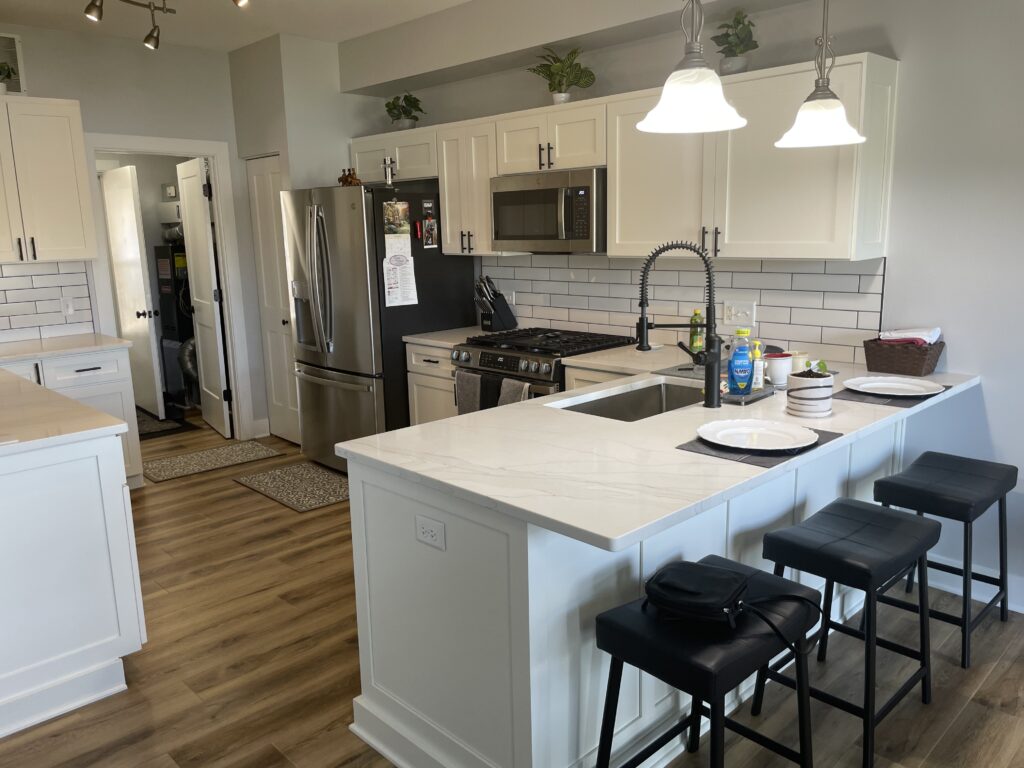 Kitchen remodel in Montgomery IL with white cabinets, black hardware, marble countertops, and vinyl wood flooring.