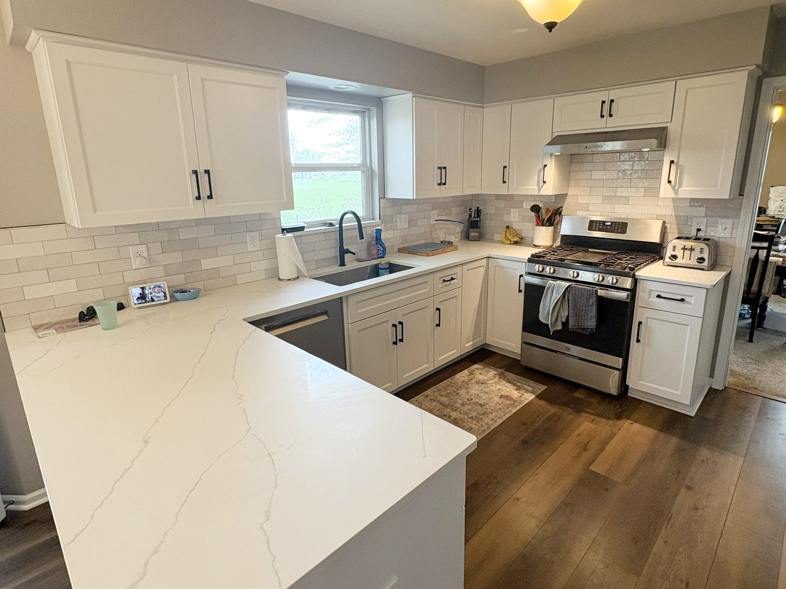 Modern kitchen remodel in Oswego, IL featuring white custom cabinetry, black hardware, tile backsplash, and durable laminate flooring.