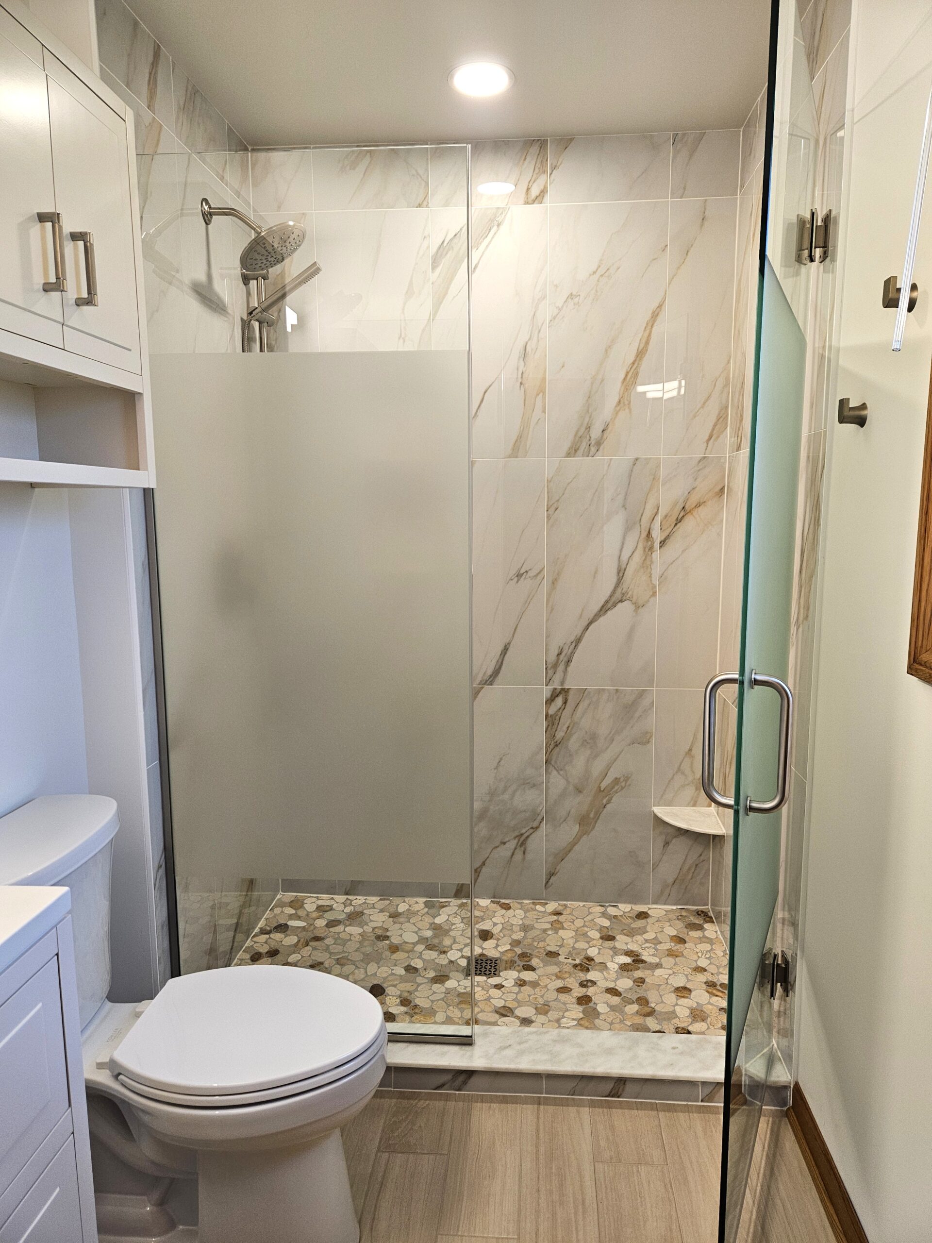 Full bathroom remodel in Orland Park, IL by NSG Construction LLC featuring a custom marble tile walk-in shower with pebble mosaic floor, frosted glass enclosure, and brushed nickel rain showerhead
